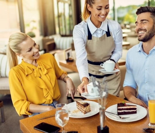 happy-waitress-serving-coffee-couple-who-is-eating-cake-cafe-min